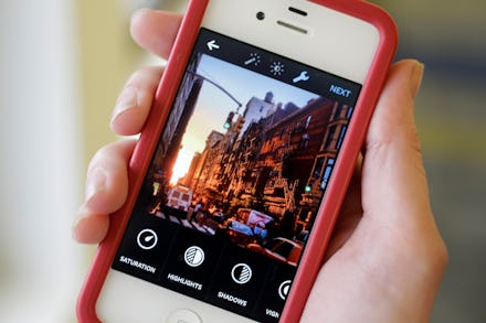 A woman holding her red-white iPhone with the Instagram app open during image editing