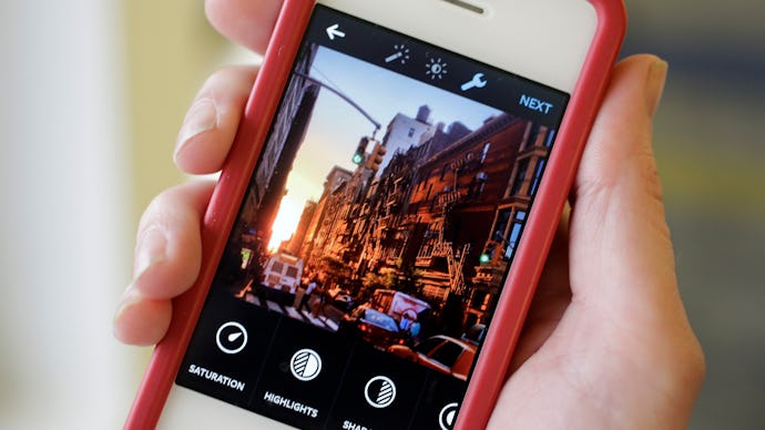 A woman holding her red-white iPhone with the Instagram app open during image editing