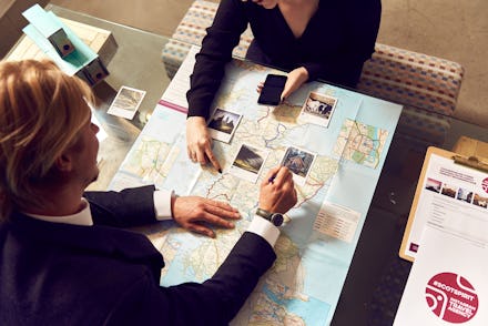 Two women looking at a world map with polaroid pictures in the world's first Instagram travel agency