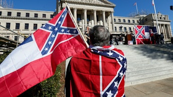 A man with two old Mississippi flags in front of the state Capitol in Jackson, Mississippi