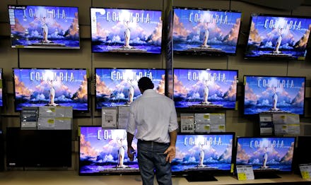 A man in a blue shirt looking at the prices of displayed TVs in a store.