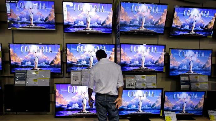 A man in a blue shirt looking at the prices of displayed TVs in a store.