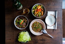 Three bowls of Taiwanese food placed on a table with chopsticks, a spoon and a drink 