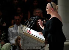 Meghan McCain in a black dress standing on a pedestal and giving a speech 