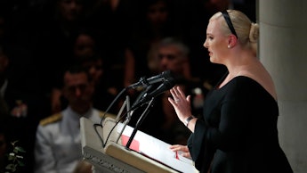 Meghan McCain in a black dress standing on a pedestal and giving a speech 