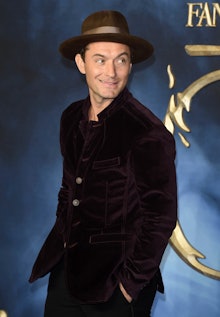 Jude Law in a black suit, and a brown hat during a movie premiere