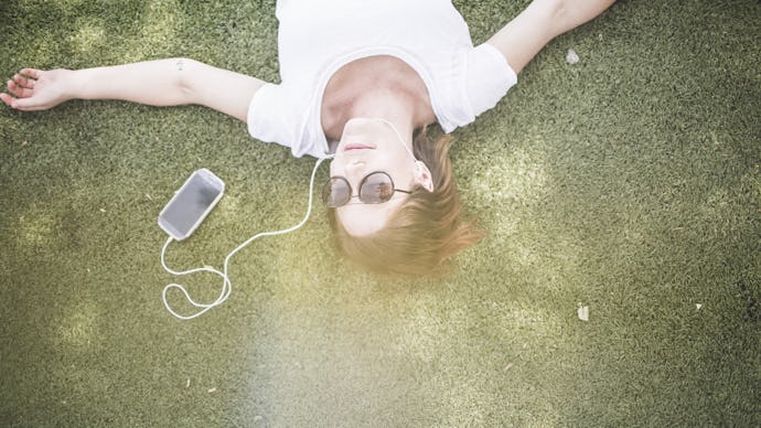 A girl lying on grass and listening to music on earphones