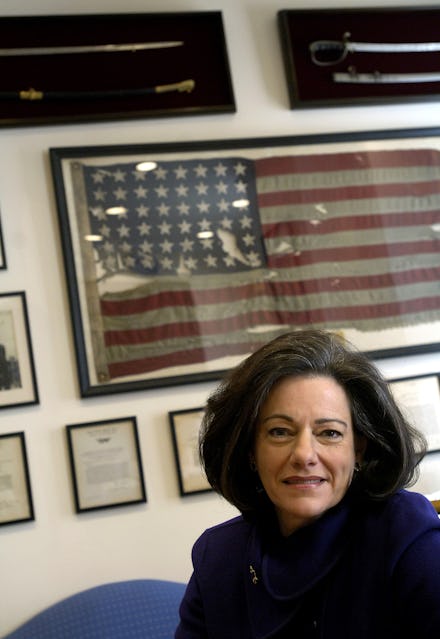 KT McFarland in a blue outfit sitting in front of a framed american flag