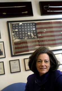 KT McFarland in a blue outfit sitting in front of a framed american flag