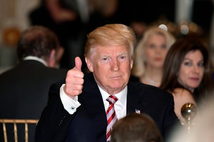 Donald Trump sitting at a table and showing a thumb up, and smiling