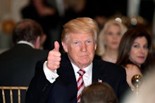 Donald Trump sitting at a table and showing a thumb up, and smiling
