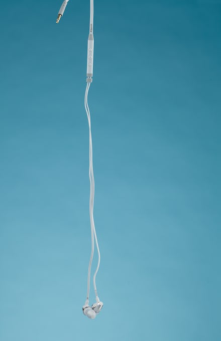 Earbuds hanging in front of a pale blue backdrop.