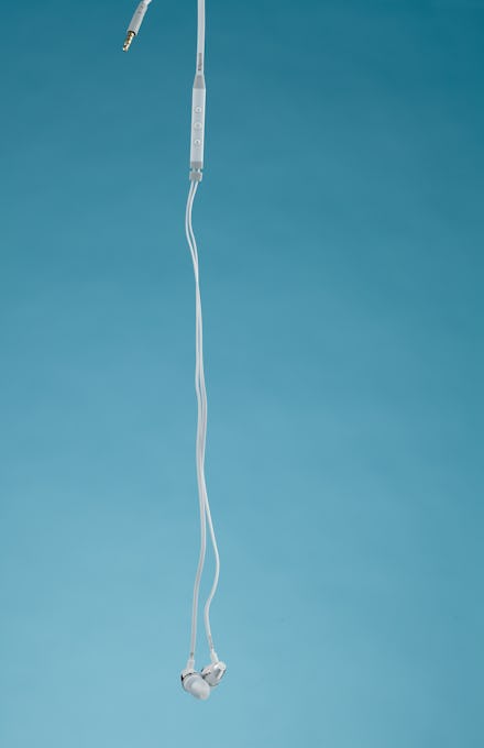 Earbuds hanging in front of a pale blue backdrop.