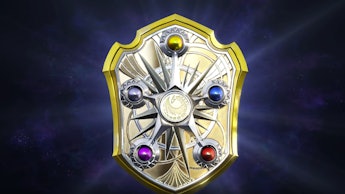 A golden 'Fire Emblem' with a yellow, blue, red, purple and grey crystal