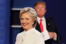 Hillary Clinton in a white blazer and Donald trump blurred in the background