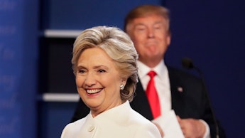 Hillary Clinton in a white blazer and Donald trump blurred in the background