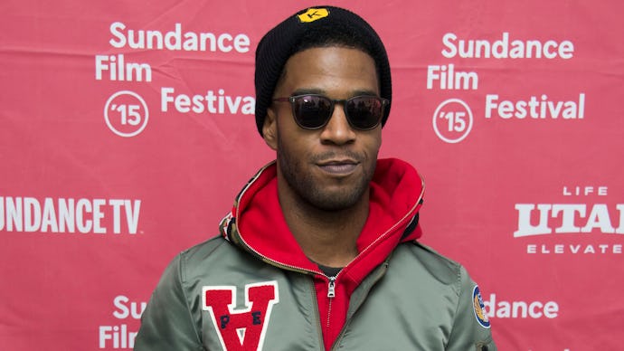 Kid Cudi posing in a green jacket, black cap, and black sunglasses