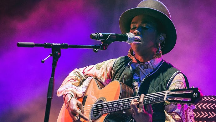 Lauryn Hill wearing a hat while playing a guitar and singing on stage