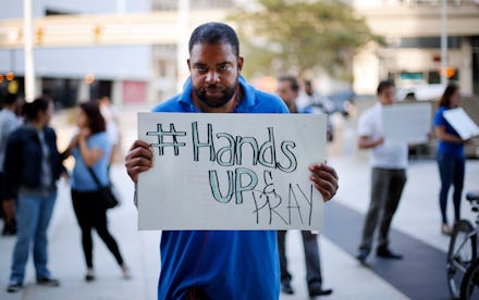 A man holding a sign that reads hands up and pray in response to the michael brown case