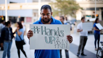 A man holding a sign that reads hands up and pray in response to the michael brown case