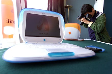 A man taking photos of three old iBook laptops