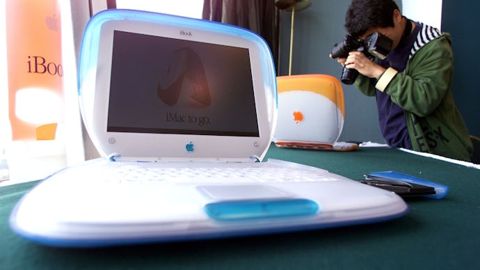 A man taking photos of three old iBook laptops