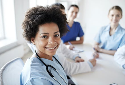 A doctor sitting next to a group of other women at a table with a stethoscope around her neck