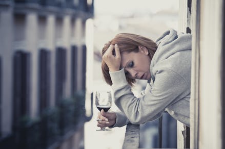 A woman leaning on her balcony railing holding a glass of wine