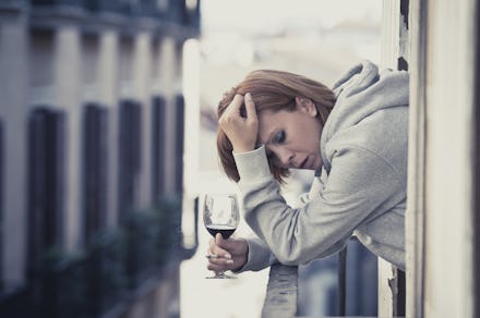 A woman leaning on her balcony railing holding a glass of wine