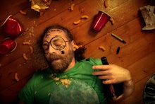 A man lying on a floor with used cups and food experiencing a hangover