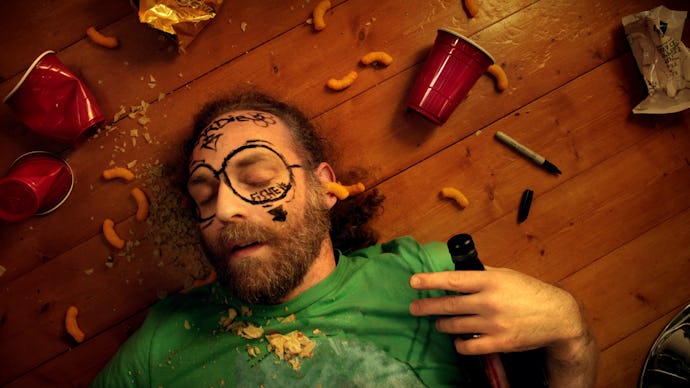 A man lying on a floor with used cups and food experiencing a hangover