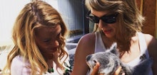 Taylor Swift and Blake Lively standing next to each other on a warm summer day holding a koala