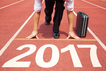 A businessman in a start position on a track field marked as '2017' with his briefcase next to him.