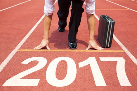 A businessman in a start position on a track field marked as '2017' with his briefcase next to him. 