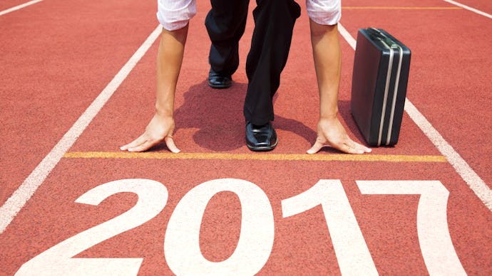 A businessman in a start position on a track field marked as '2017' with his briefcase next to him. 