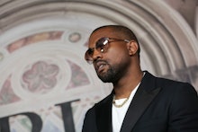 Kanye West wearing a black suit, a white shirt, a pair of sunglasses and a golden chain necklace