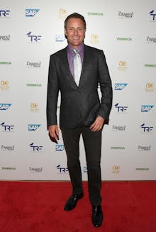 Host Chris Harrison in a grey suit, a lavender shirt, and a silver tie at a red carpet event