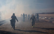 A group of migrants running after the use of tear gas at the Mexico border