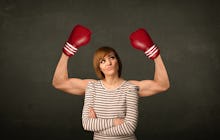 A woman in a striped shirt with her arms crossed looking annoyed while a man in boxing gloves flexes...