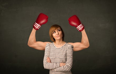 A woman in a striped shirt with her arms crossed looking annoyed while a man in boxing gloves flexes...
