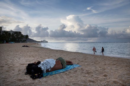A homeless person sleeping on a Honolulu beach and two other people walking