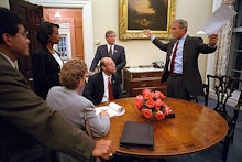 George W. Bush talking to a group of people next to a wooden table