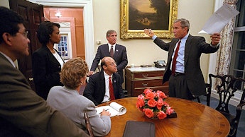 George W. Bush talking to a group of people next to a wooden table