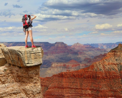 A person in climbing gear and a large backpack standing on a rock looking over the grand canyon