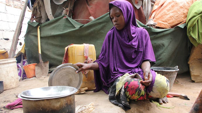 A woman in somalia crouched on the ground cooking a meal in the pot next to her