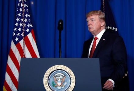 Donald Trump in a black suit, a white shirt, and a red tie walking up to a microphone stand