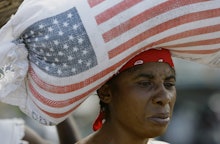 A woman carrying a heavy bag with the US flag on her head 