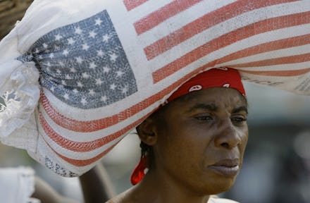 A woman carrying a heavy bag with the US flag on her head