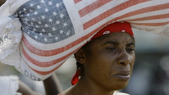 A woman carrying a heavy bag with the US flag on her head 