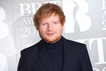 Ed Sheeran posing for a photo in a black sweater and blazer combination